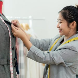 Work from home. Asian young woman fashion designer  working on her design in the showroom.  Lifestyle people Stylish tailor taking measurements on mannequin in studio.  Business small Concept